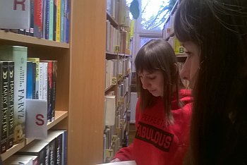 Uczniowie szukają książek wśród regałów w bibliotece