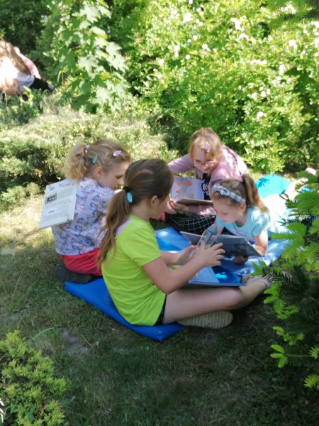4 dziewczynki prezentują sobie książki siedząc na kocu w ogrodzie.