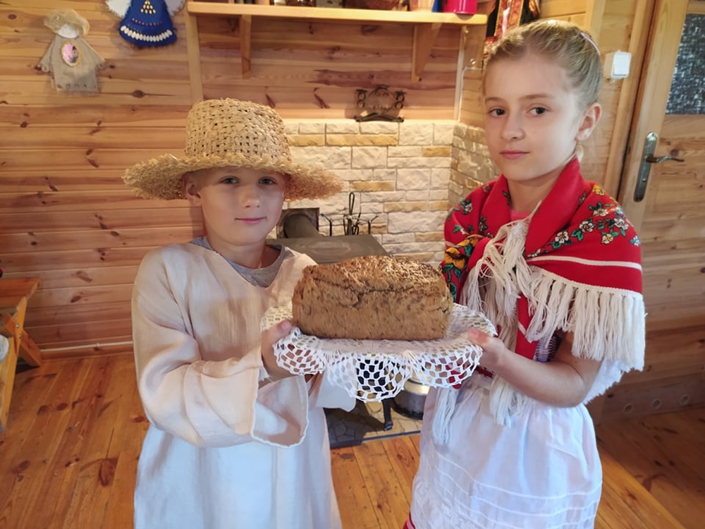 dziewczynka i chłopiec przebrani w codzienne stroje ludowe. Dzieci trzymają chleb ułożony na białej serwecie