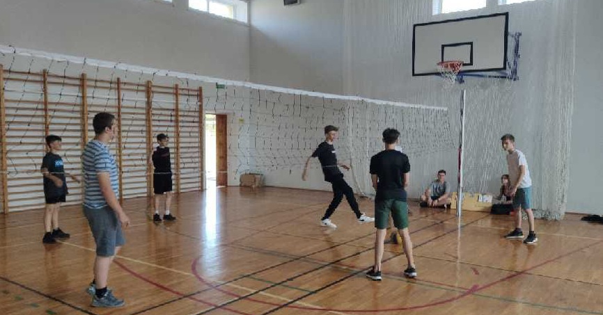 Uczniowie grający w piłkę siatkową na sali gimnastycznej