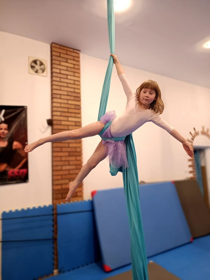 Dziewczynka w pozie gimnastycznej trzyma szarfę