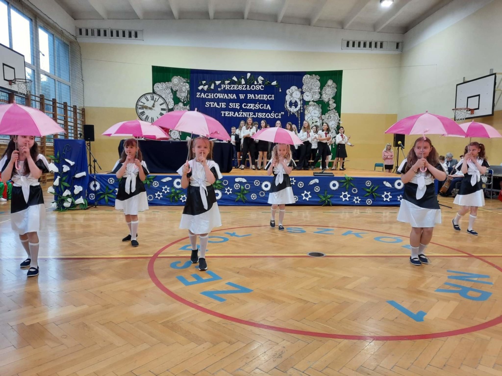 Dziewczynki tańczące w biało-czarnych strojach z różowymi parasolami. 