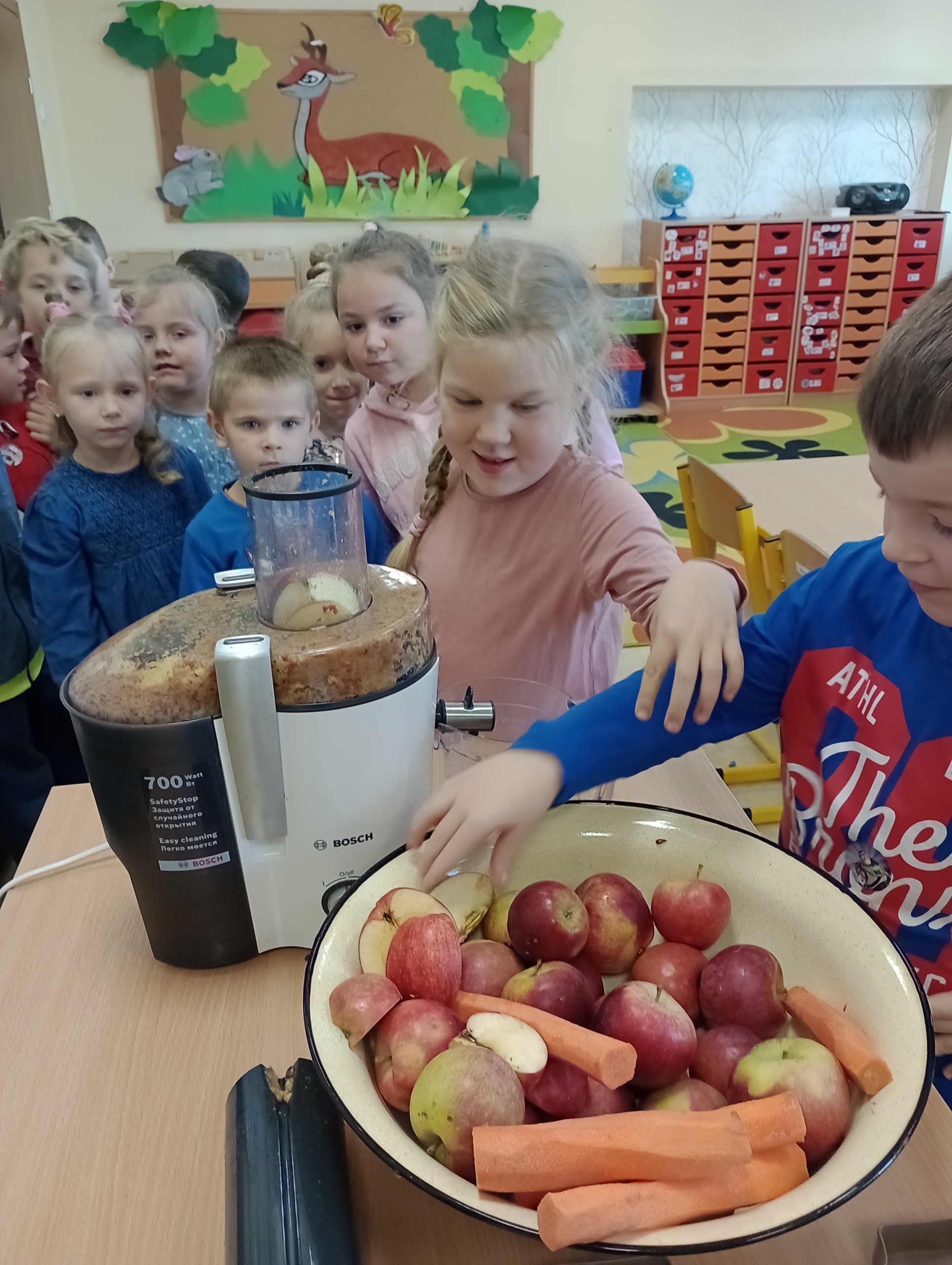 Na zdjęciu widać jak dzieci wrzucają owoce i warzywa do sokownika.