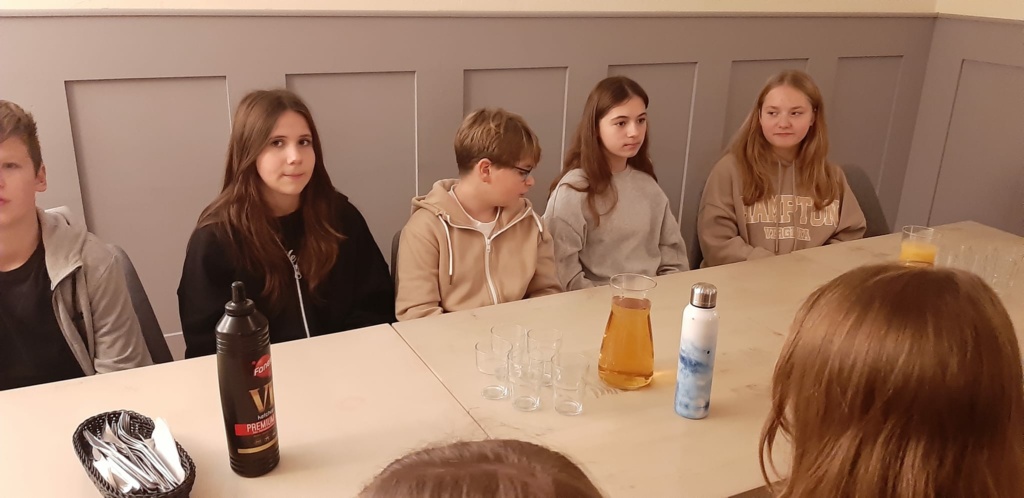 Grupa uczniów siedzi przy białym stole w restauracji.