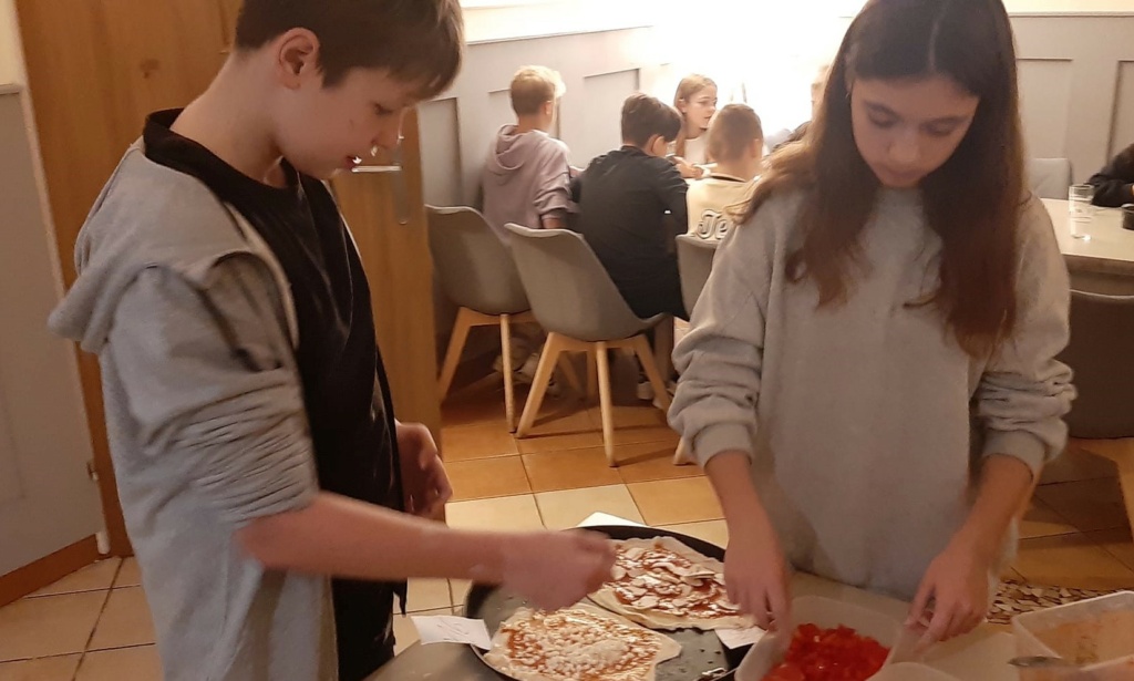 Uczniowie w parach wykonują swoją własną pizzę. Na ciasto nakładają różnorodne składniki mięsne i warzywne. 