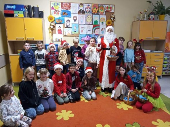 Grupa uczniów pozuje wraz z Mikołajem przy świątecznej dekoracji.