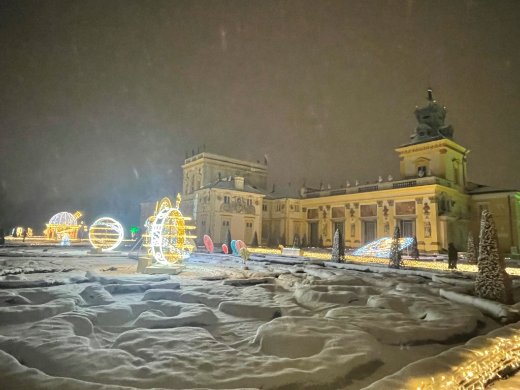 Oświetlone rzeźby stojące w śniegu, w tle widać pałac w Wilanowie