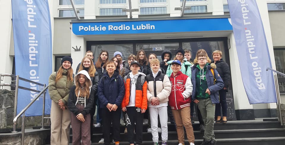 Grupa uczniów stoi na schodach przed budynkiem Polskiego Radia Lublin. Wszyscy się uśmiechają