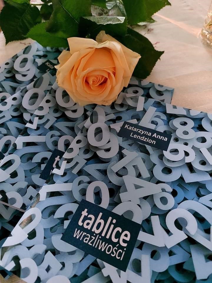 Na stoliku leżą tomiki poezji Katarzyny Anny Lendzion „Tablice wrażliwości” oraz herbaciana róża.