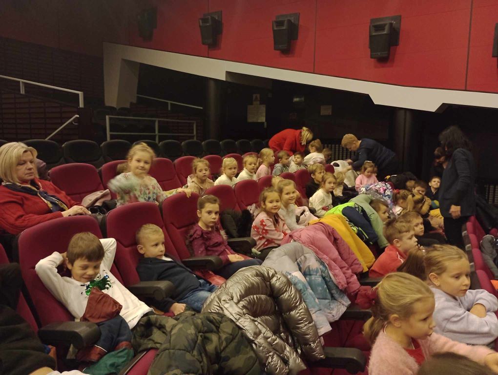 Dzieci siedzą w fotelach w teatrze czekają na rozpoczęcie spektaklu. 
