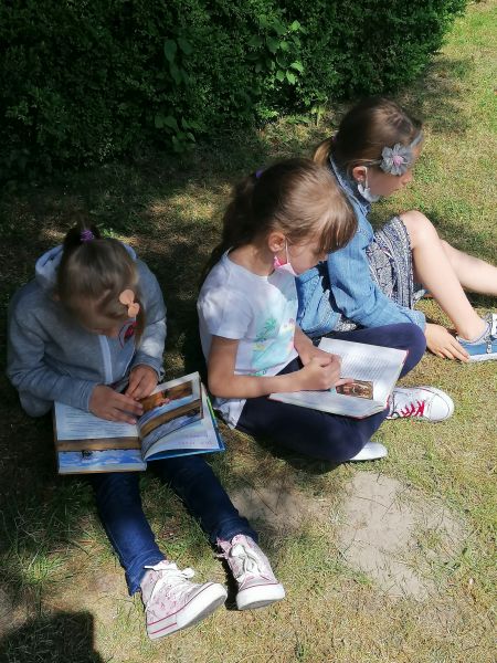 3 dziewczynki siedzą w ogrodzie w cieniu i czytają książki