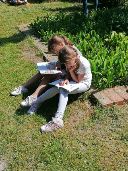 2 dziewczynki siedzą na brzegu klombu i czytają książki.