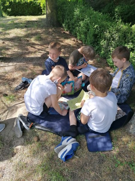 5 chłopców siedzi w ogrodzie obok siebie z książkami.