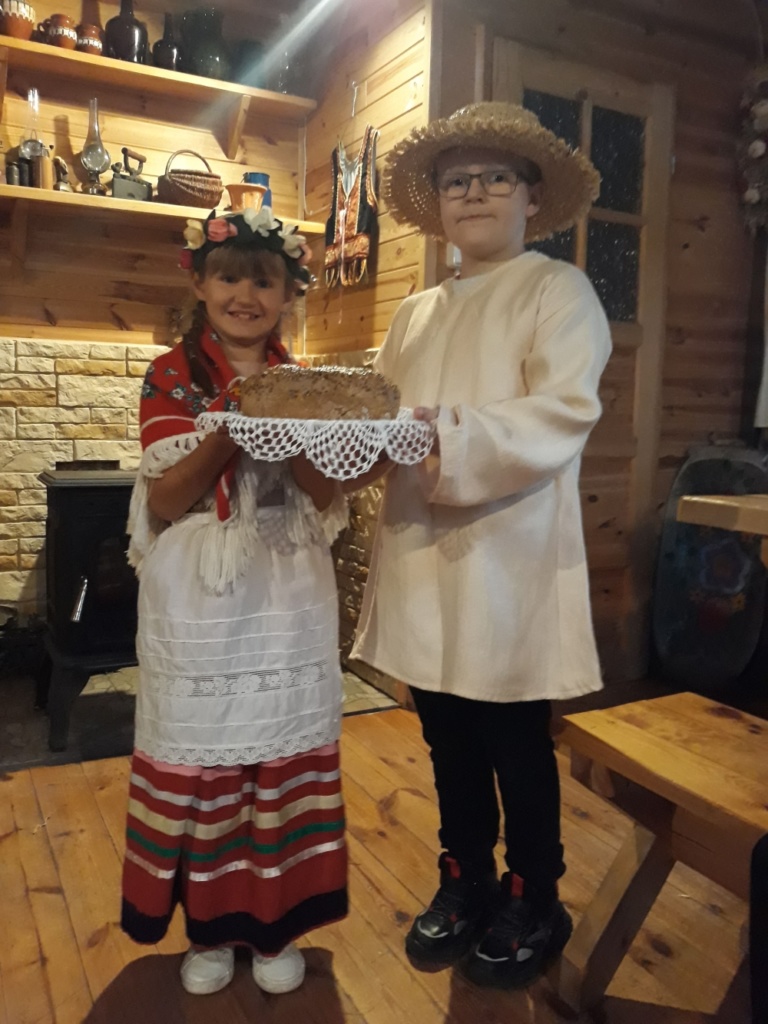 dziewczynka i chłopiec przebrani w codzienne stroje ludowe. Dzieci trzymają chleb ułożony na białej serwecie