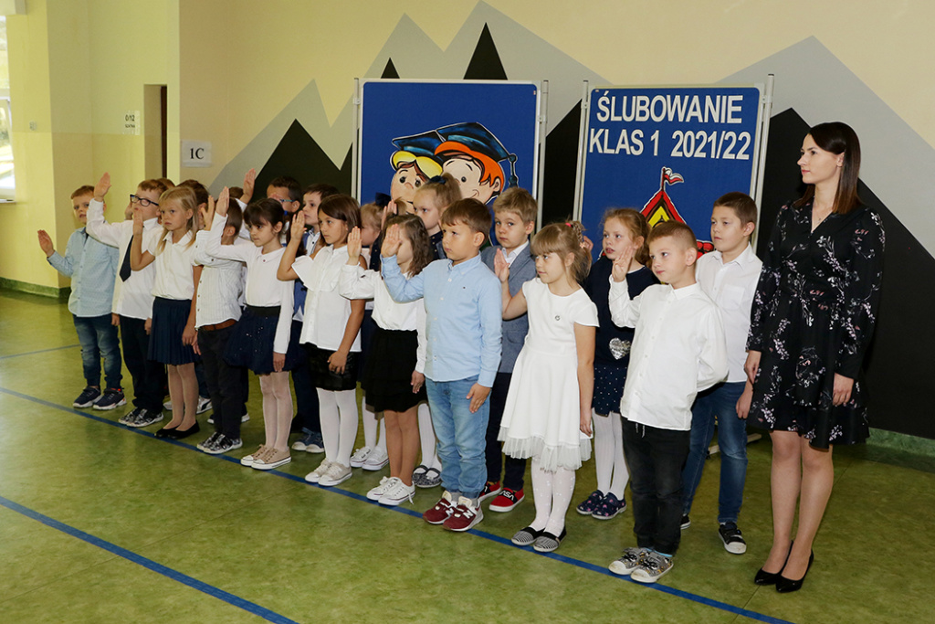 Uczniowie klasy 1E w obecności wychowawczyni składają przysięgę ślubowania. Wszyscy są dumni i podekscytowani tym faktem.