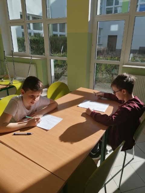 Dwaj uczniowie siedzą przy stoliku i rozwiązują zadania matematyczne.