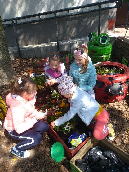 Uczniowie w kwietnym kąciku przyglądają się, jak mają sadzić kwiaty.