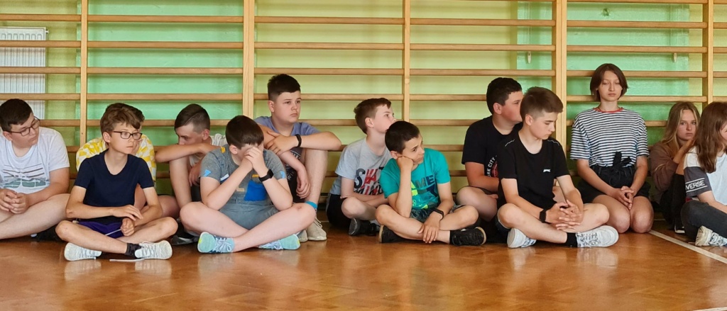 Grupa uczniów podczas spotkania na sali gimnastyczne z przedstawicielem Policji w Łęcznej