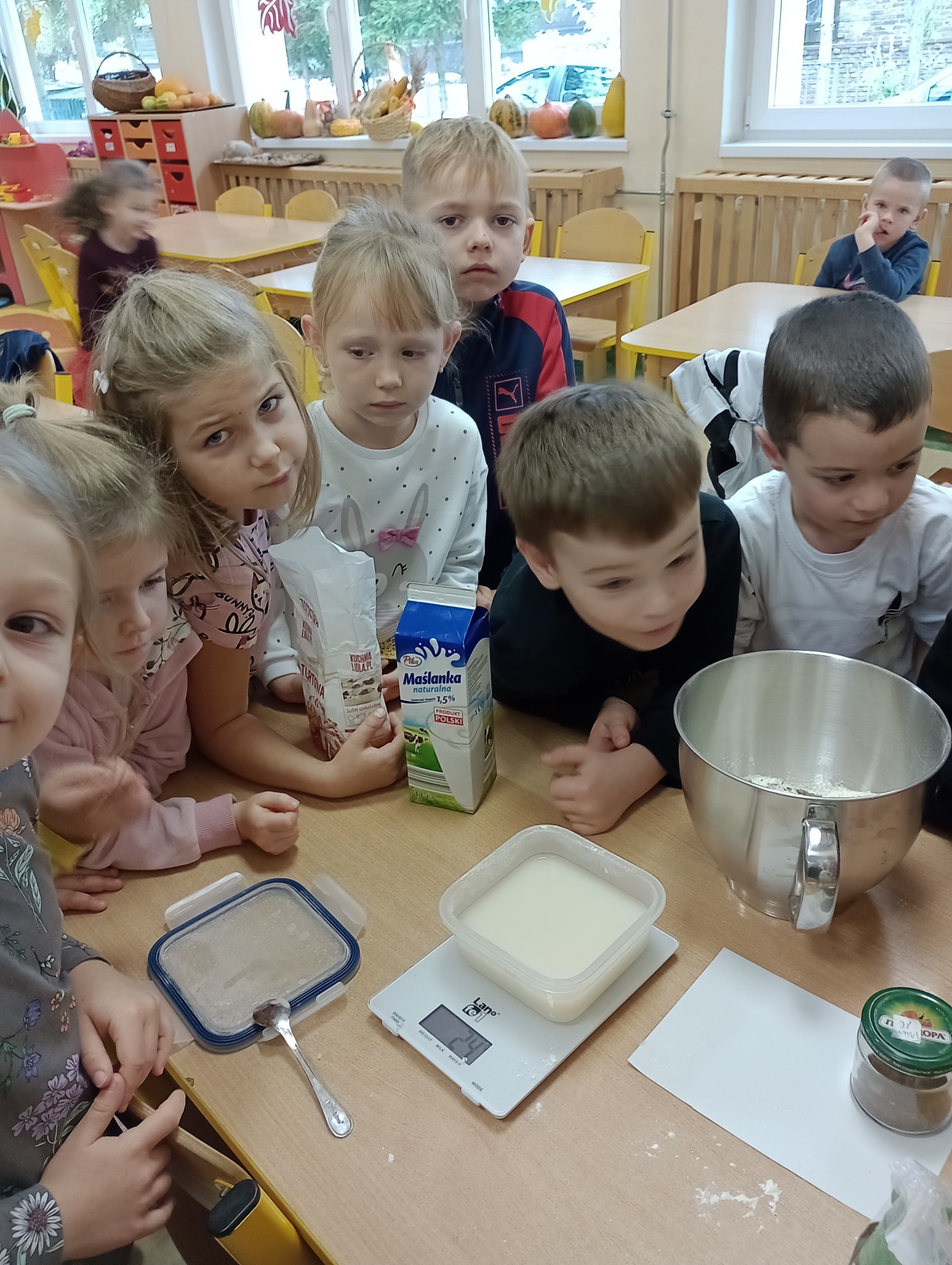 dzieci stoją przy stoliku, na którym znajdują się produkty potrzebne do wypieku chleba