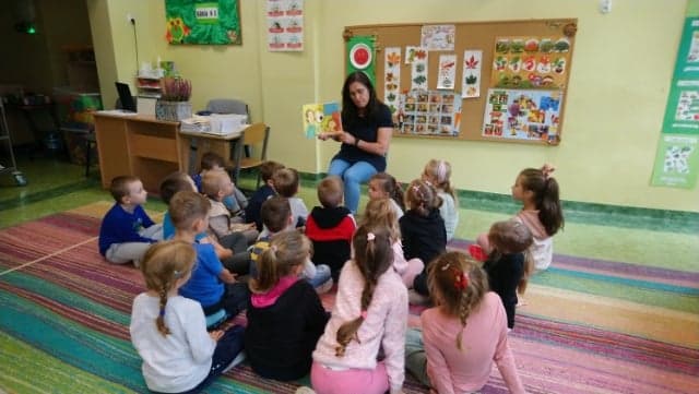uczniowie klasy 0e w trakcie słuchania czytanej książki przez panią Irenę Zaniewską