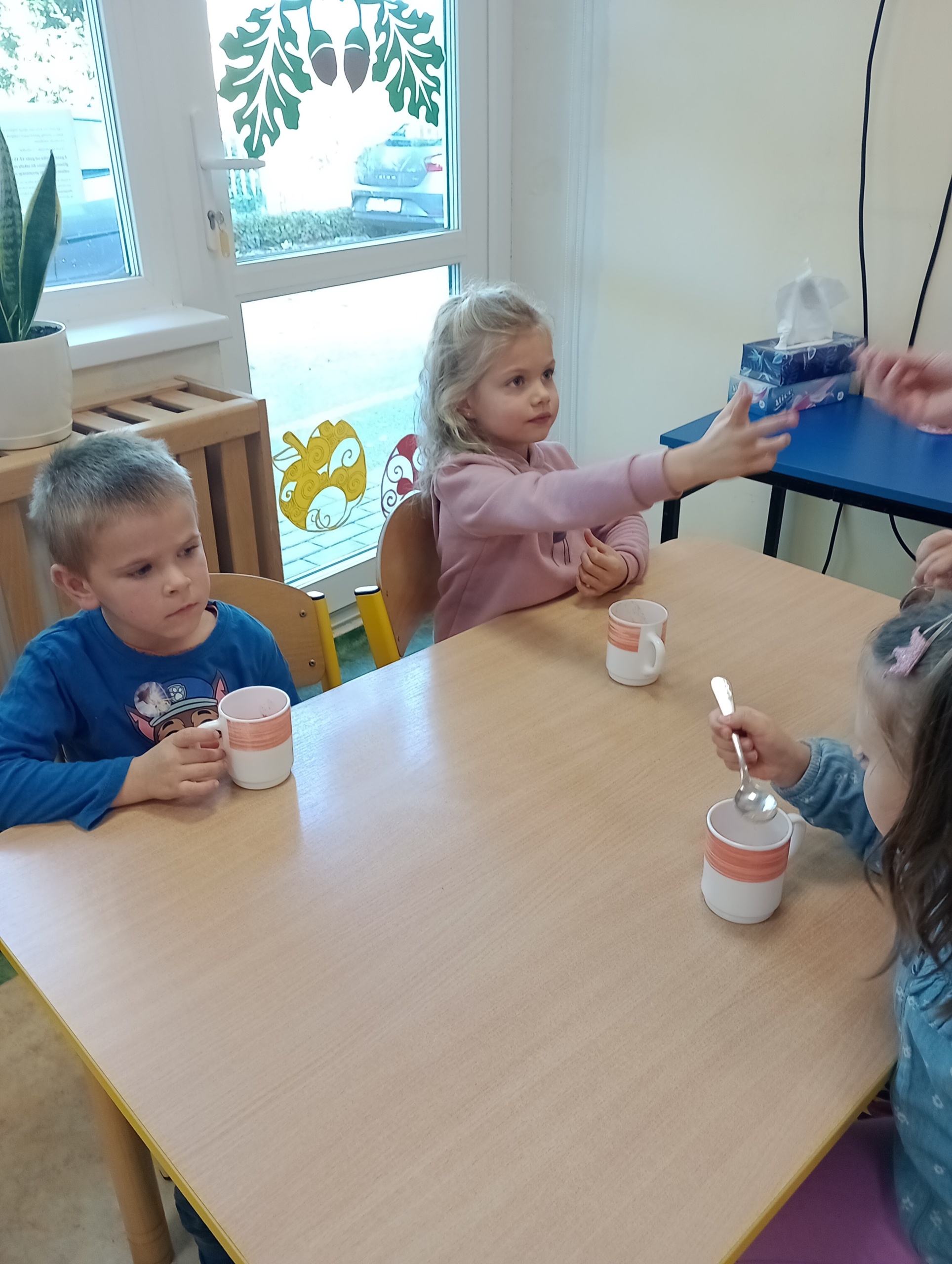 Dzieci siedzą przy stoliku i piją sok. 