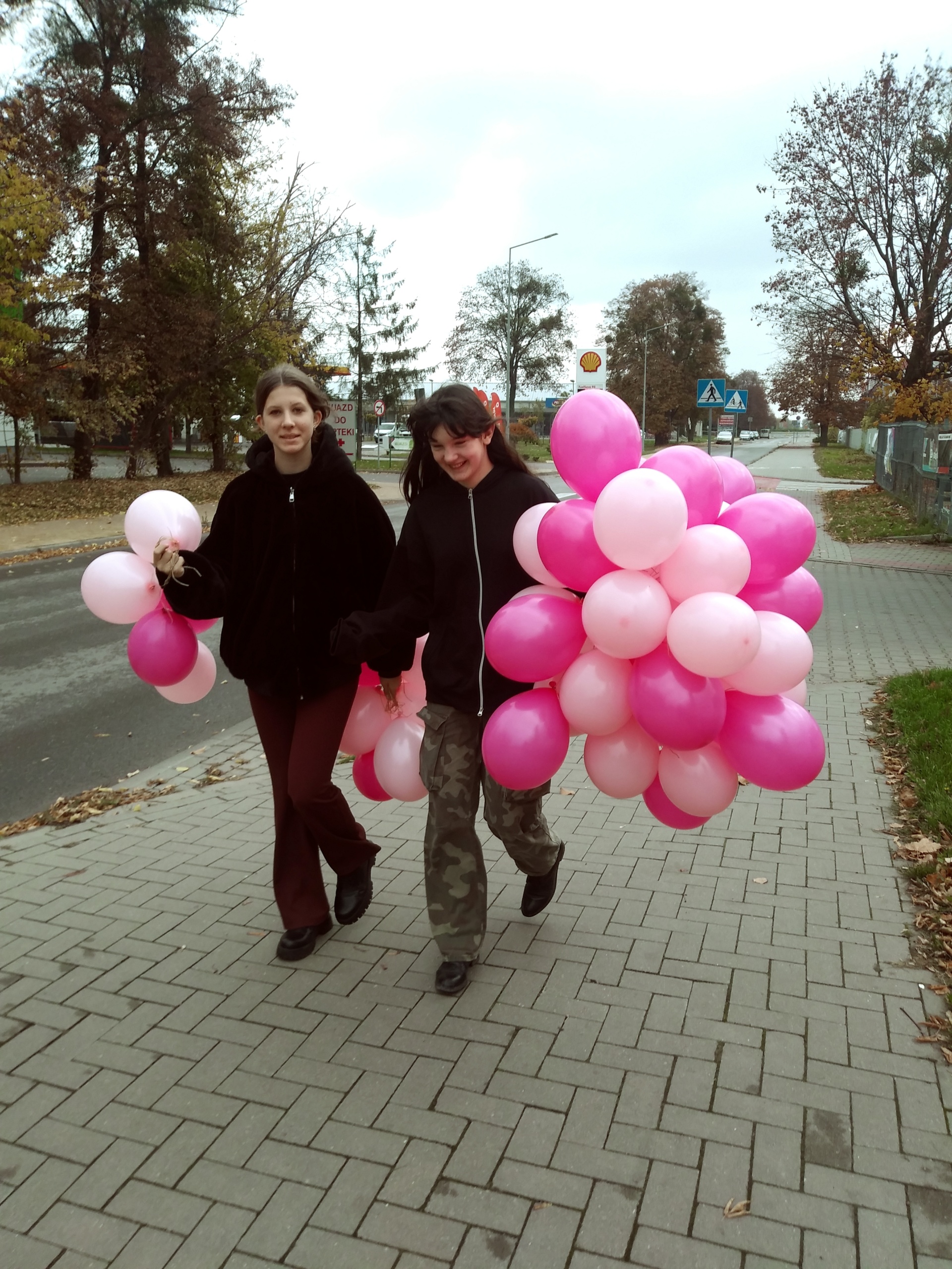 Zdjęcie przedstawia wolontariuszy idących ulicą. W rękach trzymają pęki różowych balonów.