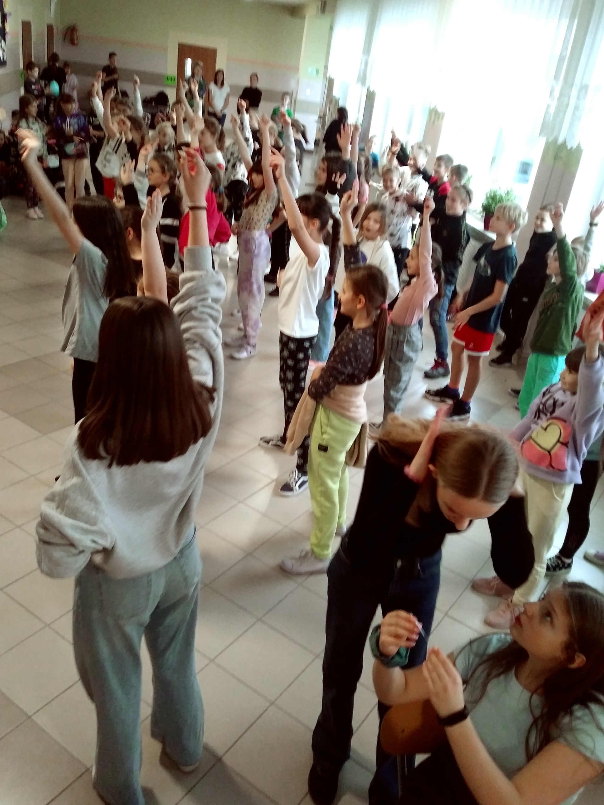 Zdjęcie przedstawia dużą grupę uczniów tańczących na korytarzu szkolnym