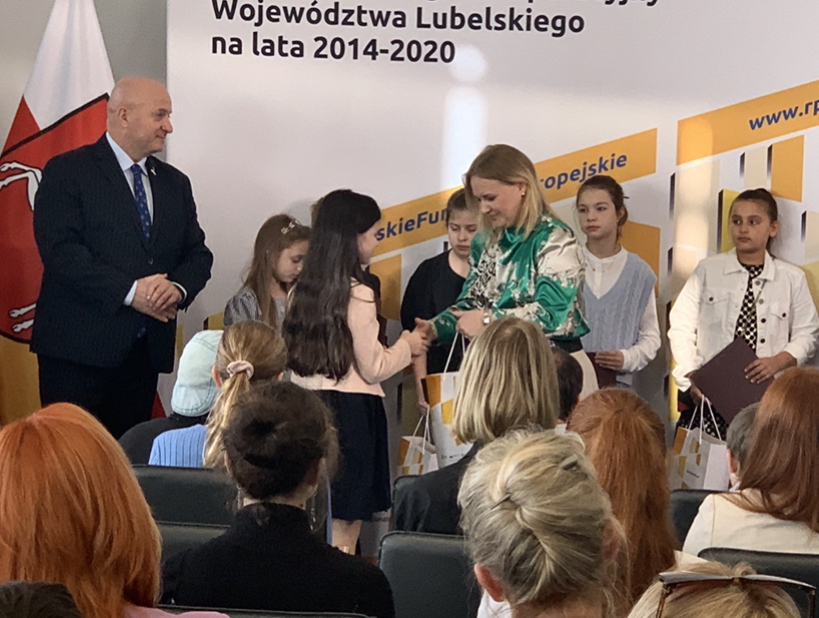 Marszałek Jarosław Stawiarski oraz Dyrektor Departamentu Zarządzania RPO Anna Brzyska wręczają dyplom i nagrodę uczennicy Julii Opajdowskiej.