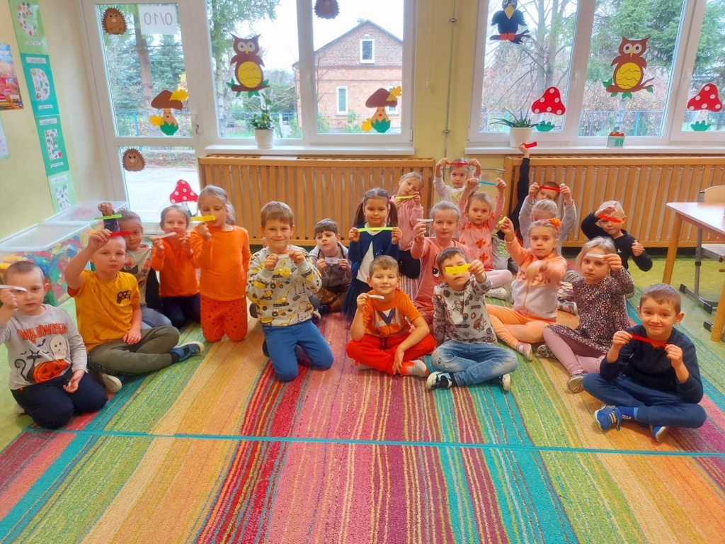 Na zdjęciu dzieci siedzą na dywanie, brane są na pomarańczowo.