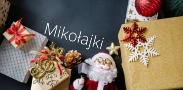 Grafika przedstawia figurkę Mikołaja pośród prezentów na ciemnym tle. Nad nimi napis "Mikołajki"