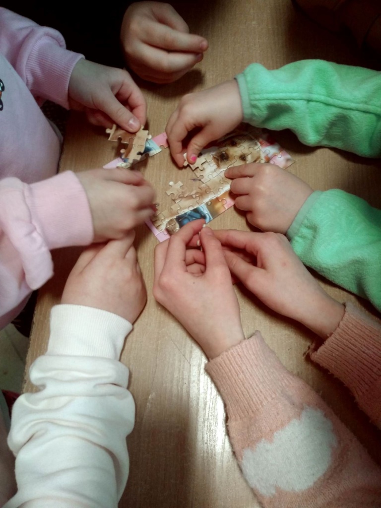 Ręce dzieci wspólnie układających jeden obrazek z puzzli.