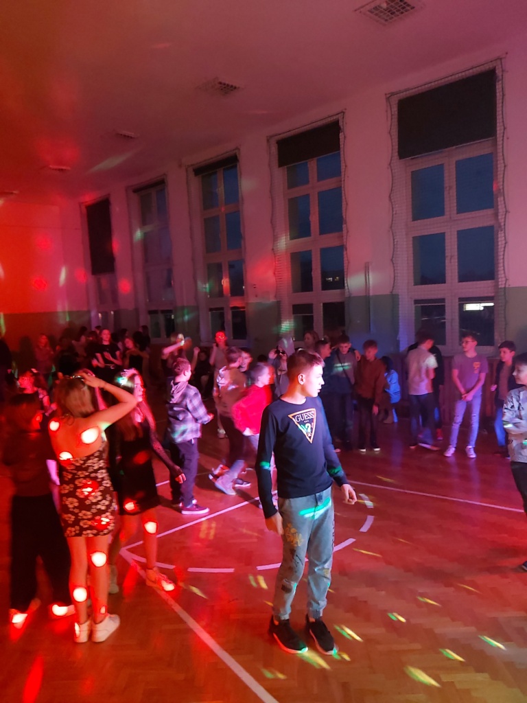 Uczniowie tańczący w rytmu muzyki na sali gimnastycznej.