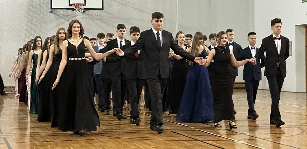 Nastolatkowie tańczą poloneza w eleganckich ubraniach, trzymają się za ręce