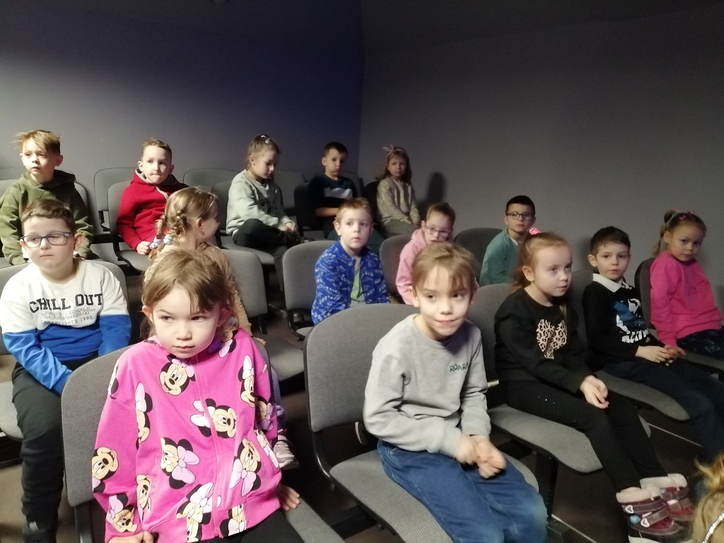  Dzieci siedzą na krzesłach i oglądają film w kinie.