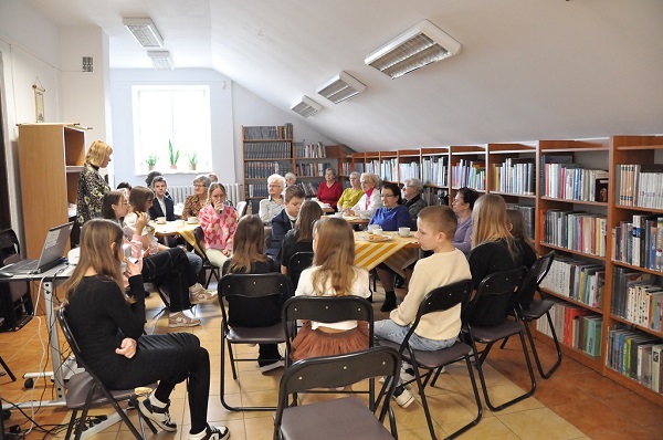 Ucznioweie wraz z seniorami w wspólnie biesiadują w bibliotece.