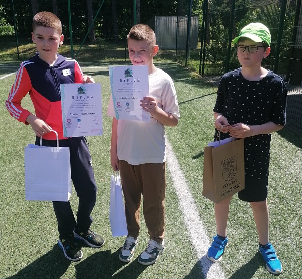 trzech chłopców stoi na boisku szkolnym w ręce trzymają dyplomy
