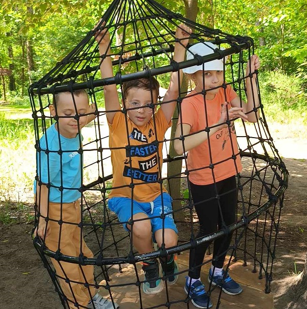 troje dzieci huśta się w klatce z siatki w lesie