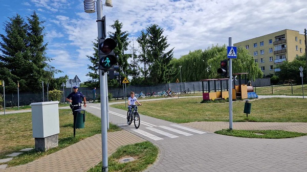 Chłopiec jedzie na rowerze po miasteczku rowerowym, obok idzie policjant w mundurze.