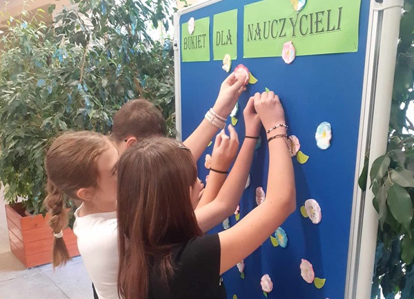Uczniowie przypinają kwiatki do tablicy i tworzą bukiet.