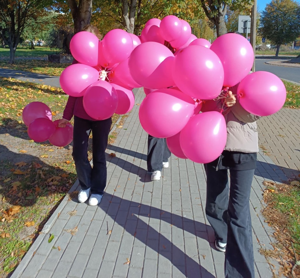 trzy dziewczyny idą, trzymają różowe balony, w tle jesienne drzewa