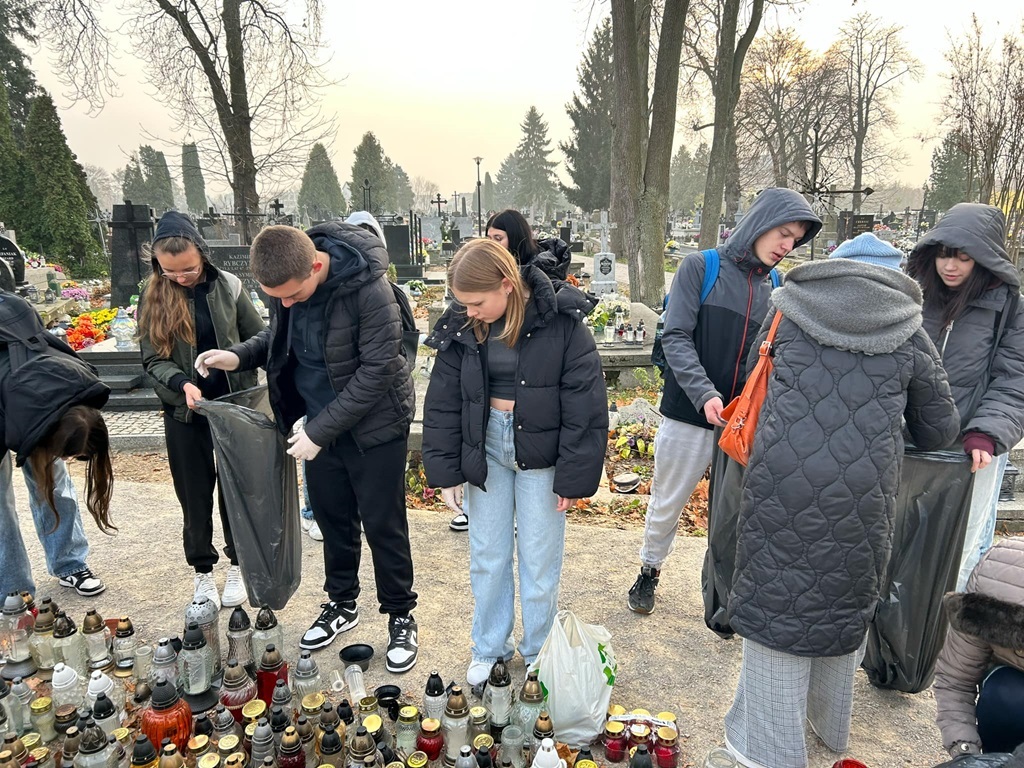 uczniowie i nauczycielki zbierają wypalone znicze przy grobie żołnierzy.