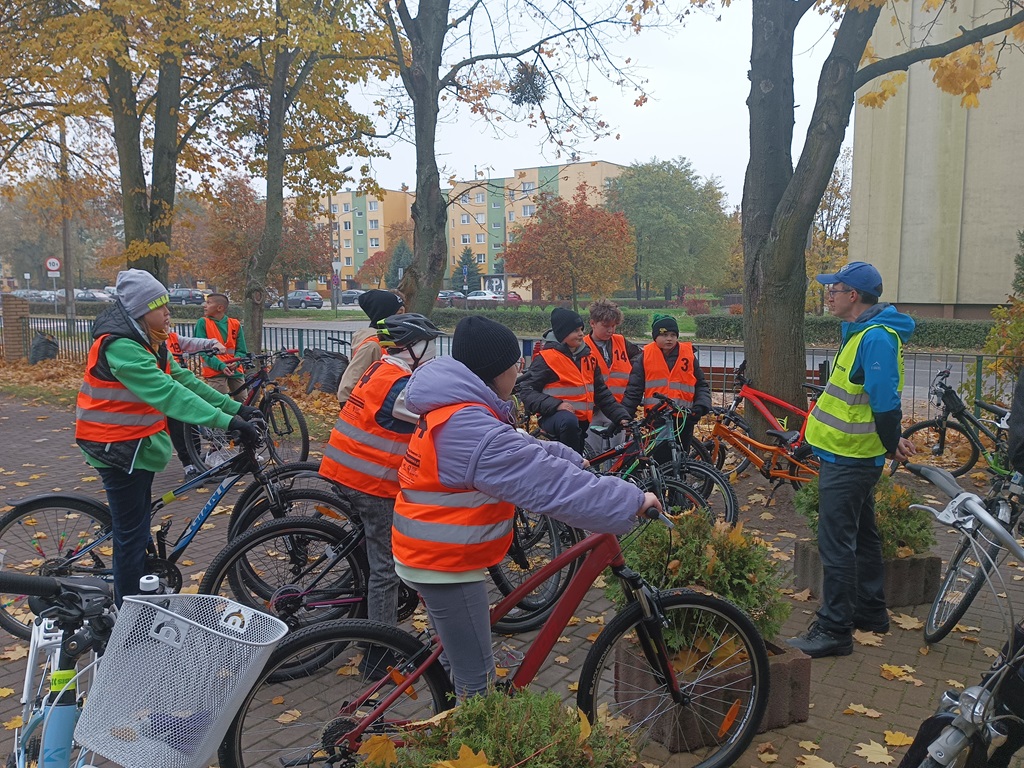 uczniowie siedzą na rowerach i słuchają instruktażu osoby dorosłej