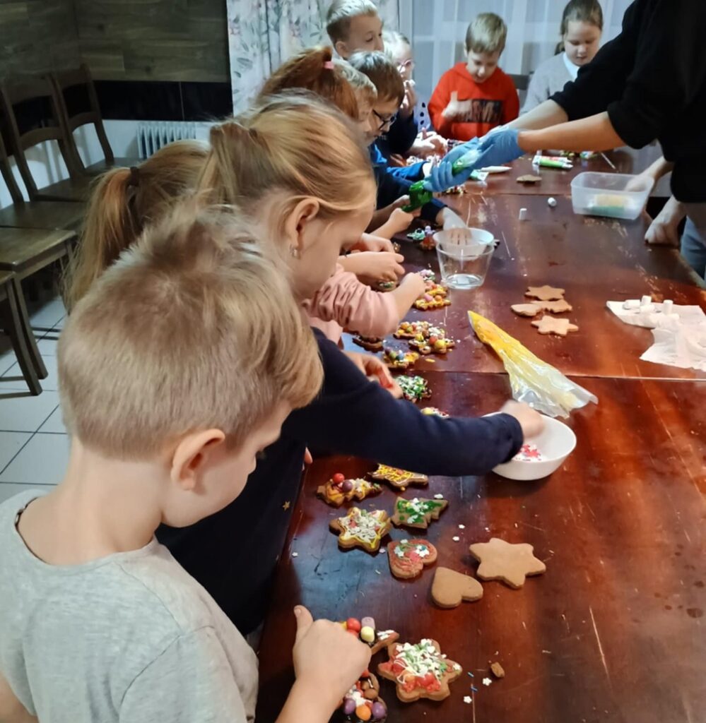 Dzieci uśmiechnięte dekorują upieczone pierniczki.