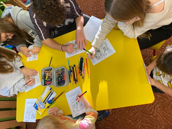 wolontariusze i przedszkolaki kolorują ilustracje przedstawiające owoce