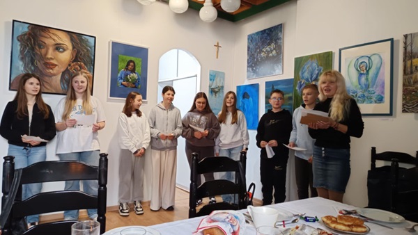 wolontariusze i nauczycielka śpiewają w domu kultur, z przodu stół nakryty białym obrusem