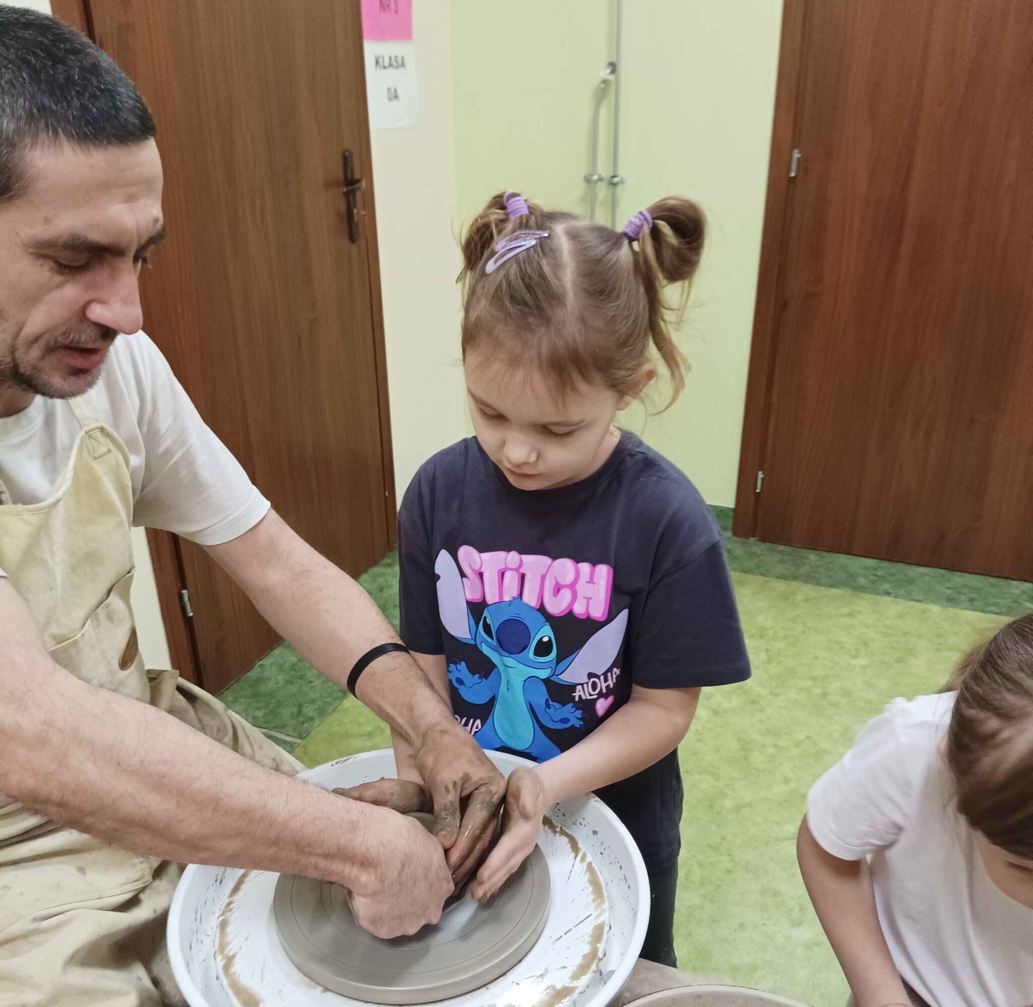 Uśmiechnięta dziewczynka formuje miseczkę na kole garncarskim.