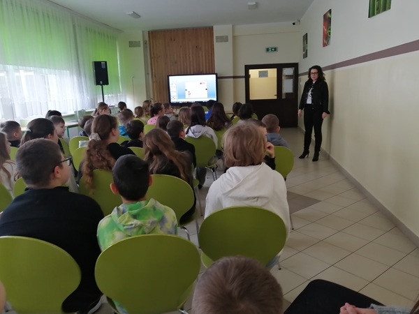 Grupa uczniów siedzących i patrzących w stronę prelegenta. W tle tablica interaktywna.