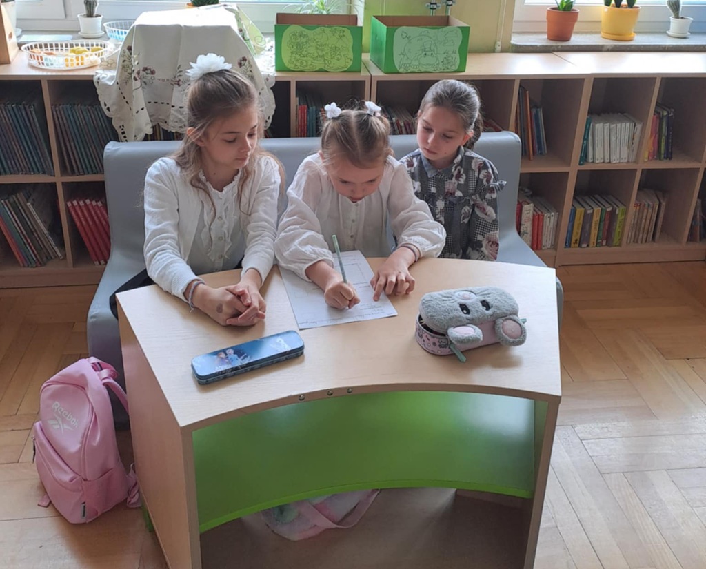 trzy dziewczynki siedzące przy stoliku i rozwiązujące test