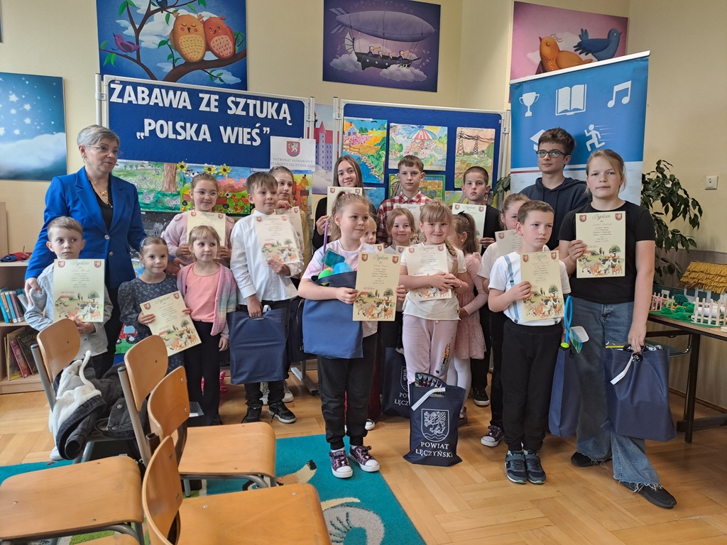pani dyrektor i laureaci konkursu trzymający nagrody i dyplomy na tle prac konkursowych