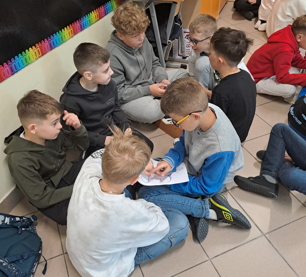 Dzieci siedzące w grupach i trzymające kartki.